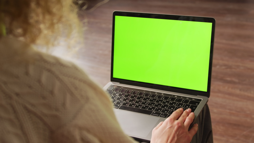 Handheld slow motion over the shoulder shot of a curly woman holding a laptop with a green screen chroma key on her knees | Shutterstock HD Video #1069213321