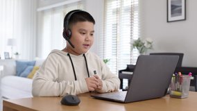 Young asia boy student wear headset headphone with computer laptop videocall talk present online e-learning class study with teacher, social distance learn language at home, homeschooling concept.