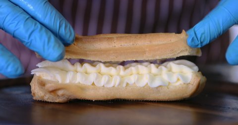 Chef with confectionery bag stuffing the eclair with choux cream. Homemade eclairs. Squeezing vanilla cream in eclair and profiteroles. The filling for the eclairs extruded from a pastry bag.