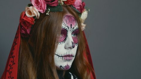 woman in the image of death Santa Muerte or sugar Mexican skull poses at the camera, revealing her face with her hands. halloween makeup, close-up.