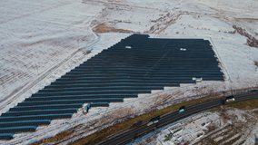 Aerial view of solar panels farm or factory on snowy hill near road with driving heavy trucks and commercial car in winter. Drone shoots video of energy saving and concept of alternative power source