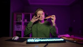 Hungry gamer streamer eats pizza with delivery and plays video games at home on computer at night. Guy eats pizza at the computer at home.