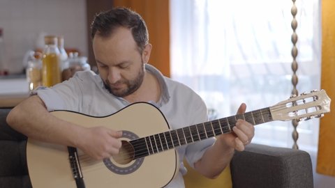 The bearded young man having fun alone playing the guitar at his home. The concept of having fun alone. Portrait of lonely man playing guitar. Slow motion video.Close up.