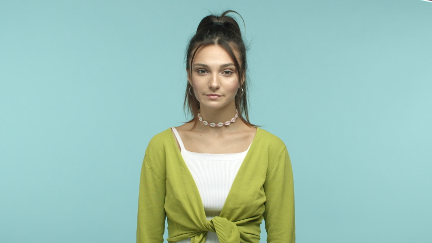 Slow motion of beautiful and cheerful young woman feeling joy, smiling carefree and shaking head relaxed and upbeat, standing over blue background