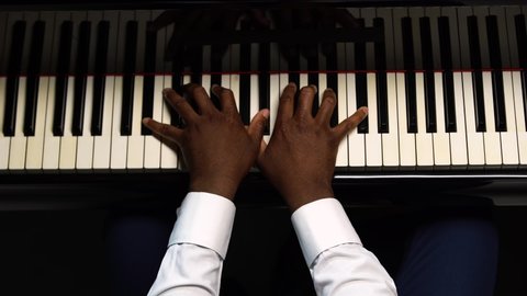 Top view of male hands playing the grand piano. The African American touches the black and white keys with his fingers to create the rhythm of the melody. Close up black hands of a male pianist.