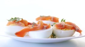 halves of boiled eggs with pieces of salted salmon on white background
