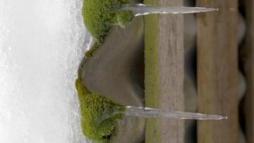 Closer look of the melting ice on the roof of the small wooden cabin with the green moss on it in Estonia vertical video