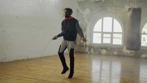 African american man skipping the rope in an empty hall, listen music