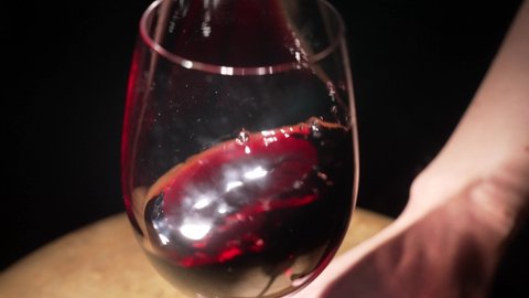 This slow motion video shows a close up view of red wine being swirled in a glass to release aromas.