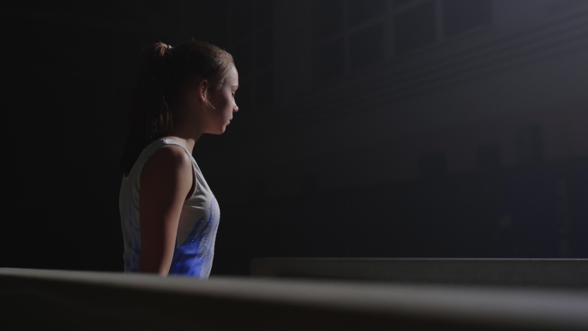 young female sportsperson in dark gymnastic hall, training with balance beam, artistic gymnastics, sport and youth