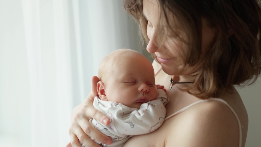 Mother holding a newborn baby in her arms. Young mother is keeping in arms and caressing her newborn baby. | Shutterstock HD Video #1069234771