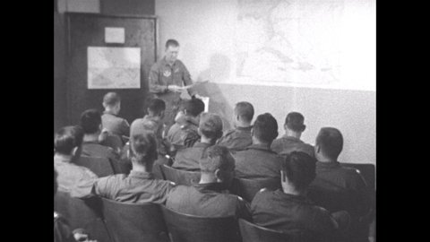 1960s: Airmen in flight suits file into classroom and sit. Man at front points to map of Cuba, Florida and Haiti,Dominican Republic.
