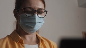 girl in a medical protective mask works at a laptop in the office. Stay home social video call distance coronavirus concept. Woman in medical protective mask working home. social distance