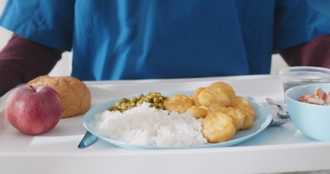 Close up of nurse carrying tray with hospital food for patient in hospital. Cropped shot of male prisoner holding tray with meal walking indoors