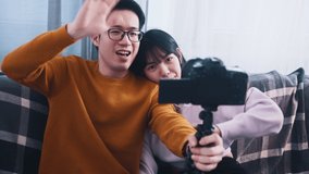 Young happy asian couple waving to the camera. Influencer streaming from the home. High quality 4k footage