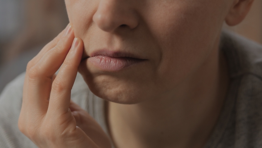 Close-up of a distressed woman with a toothache and her hand touching her face. The concept of dental disease | Shutterstock HD Video #1069250497