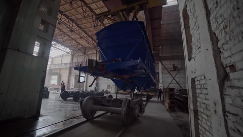 A factory crane puts a blue carriage on a railroad wheel in a modern carriage plant. Under the strict control of mechanics, a huge railcar is being prepared for future operation. Railcar manufacturer