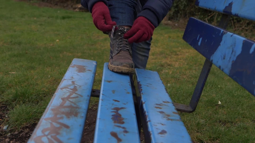 Hiker ties boot laces on neglected bench in urban park 