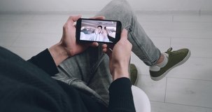 Close-up man watching internet video with popular videoblogger on his smartphone. Young male student using mobile phone for online video calling, while sitting indoors at home.