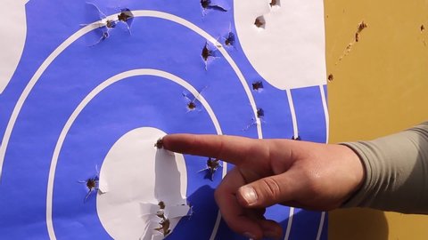 A shooting gallery, a man points a finger at the inlets from bullets hitting the target.