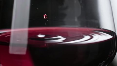 Glass with slowly falling drops. Close-up of wine drop falling into red wine. Slow motion of pouring red wine into goblet.