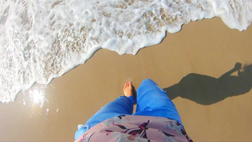Slow motion of Sea waves washing over female feet, Young woman standing on seashore and enjoying tides of sea on trip, enjoying summer vacation at seaside. Top View POV 