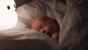 newborn baby boy sleeping in bed in the evening, face of 3-week-old infant in light of a night lamp.