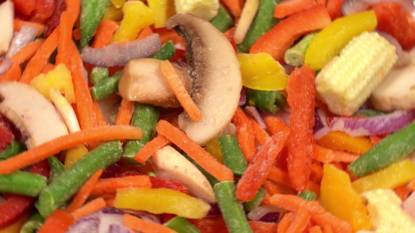 Closeup view 4k stock video footage of mixed frozen icy fresh raw vegetables rotating on white big plate isolated. Organic vegetables background