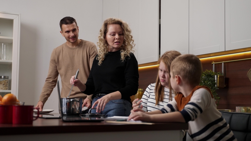 Hearing impaired teen girl with elementary age boy doing homework at laptop and communicating using sign language with mom and dad. United deaf-mute family during non-verbal conversation in kitchen