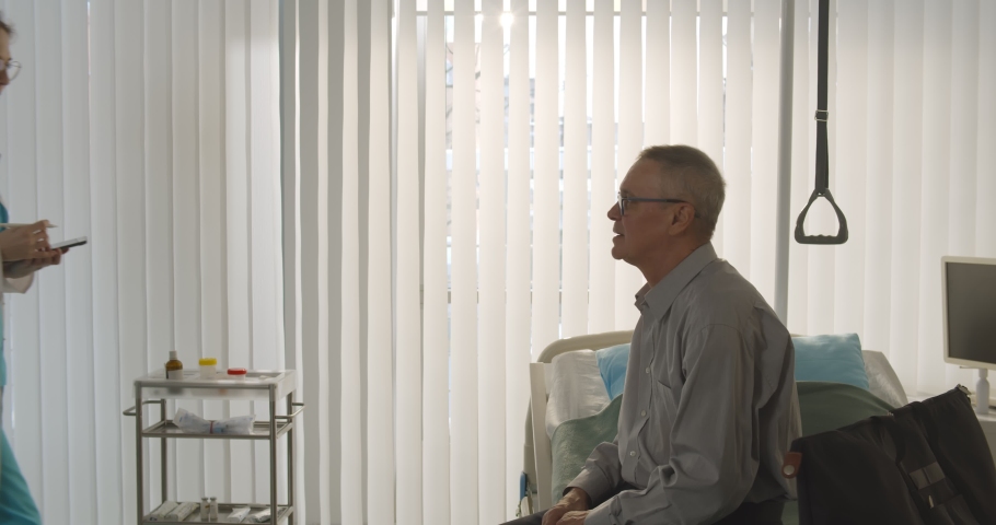 Aged man patient sitting on bed in hospital ward and signing discharge form. Side view of doctor giving document to senior male patient to sign and discharging him after full recovery Royalty-Free Stock Footage #1069268521