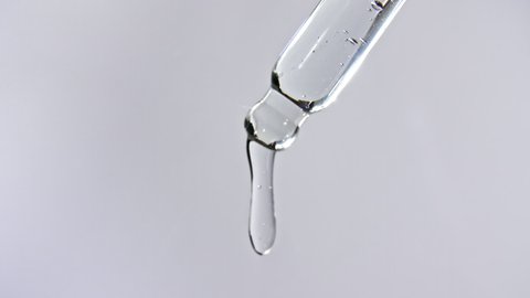 Cosmetic pipette with drops of oil close up on gray background