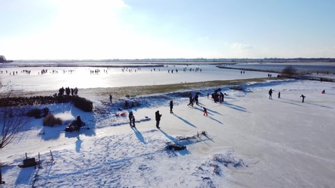 Flying towards the sun on this amazing cold winter day. Many people go outside on the frozen lake to ice skate. A 4k cinematic drone shot made in Akersloot, Europe.