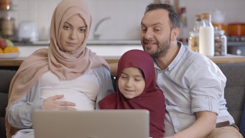 The Muslim woman wearing a hijab is happy when her daughter and husband video chat with their family and show her belly for the baby to be born. New sibling concept.Close up.
