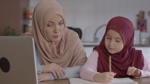 Mother with a turban is helping her daughter who is receiving distance education.Distance education by computer. Online education concept.Close up.