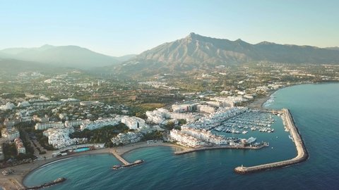 Aerial perspective of luxury and famous Puerto Banus marina, situated in Marbella, Costa del Sol. Sunset colours, Sun going down reflecting warm colours on buildings. Drone going forward. 