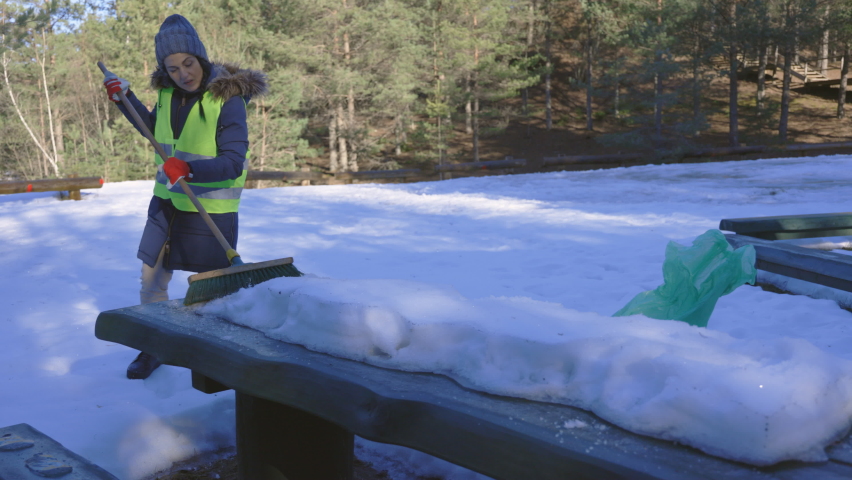 Woman volunteer try to removing snow covered table in camp place
