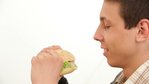 CLOSE UP. A hungry man holding a hamburger widely opens his mouth and eats a piece.