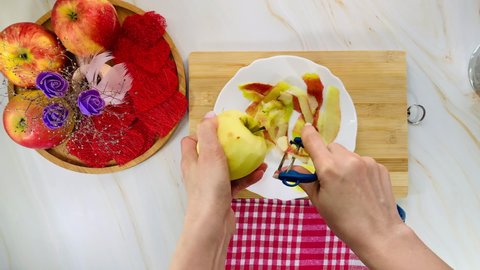 Woman peels apples. Red apples on a wooden dish. Prepare apple dessert.