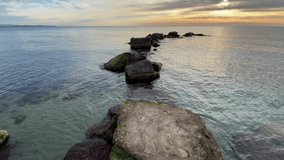 view of a beautiful calm sunrise on the beach with a rock path in the water
