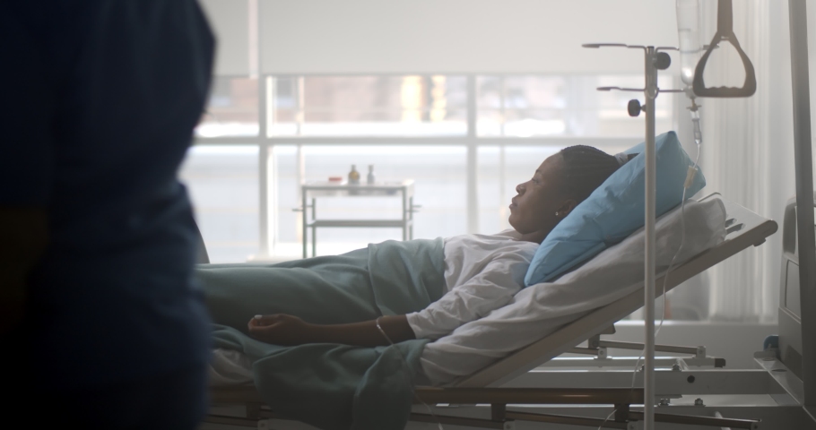 African male doctor checking up female patient in hospital ward. Side view of black man practitioner talking to sick young woman lying in hospital bed and writing down in clipboard Royalty-Free Stock Footage #1069293526