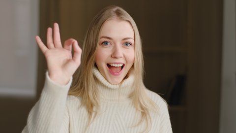 Portrait of attractive young caucasian millennial girl smiles at camera showing hand OK sign. Blonde woman shows everything fine success gesture body language, demonstrates symbol of support approval