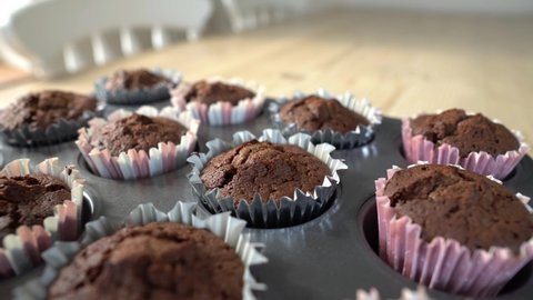 Slow motion horiztontol pan of baked chocolate cupcakes. Sitting in muffin tray on cooling rack in preparation of decorating. Home baking concept.