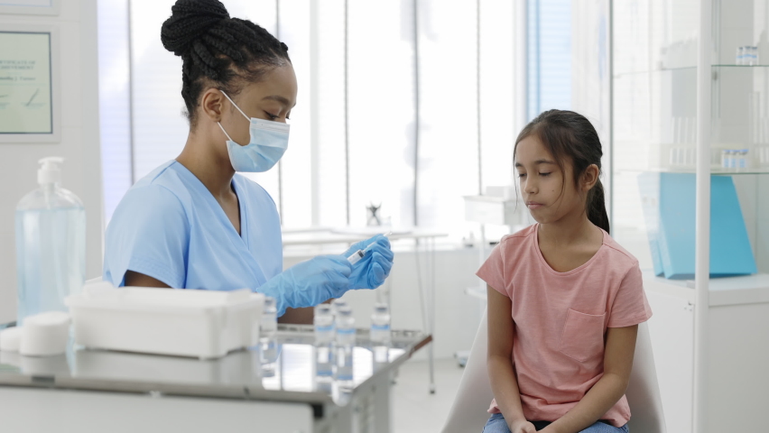 Little kid watching how doctor in protective mask and safety gloves filling syringe with vaccine in hospital while waiting for vaccination. Concept of health care, prevention. | Shutterstock HD Video #1069304038