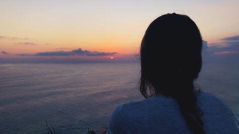 Silhouette of a woman with tropical sunset above the ocean.	
