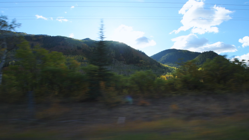 Side pov point of view car vehicle driving at Castle Creek scenic winding curve road with red yellow aspen trees in colorful autumn with sunny sun hiding behind mountains by rural countryside farm Royalty-Free Stock Footage #1069306954