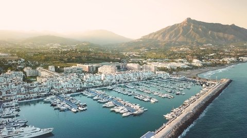 Panoramic aerial view of "Puerto Banus" Bay. Beautiful warm colours at sunset. Luxury and famous destination in Marbella. La Concha mountain in background. Drone panning left and going backward
