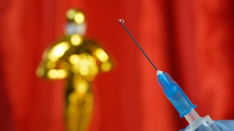 syringe with vaccine against covid-19 on hollywood Golden Oscar Academy award statue on red background. Success and victory concept. Oscar ceremony