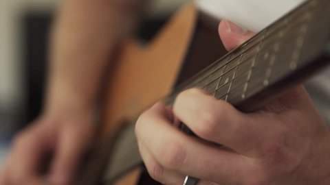 Young married man practicing acoustic guitar in his living room. close up of hand.