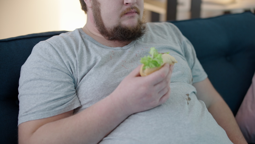 Messy plus size man chewing unhealthy sandwich, wiping hand on T-shirt, hygiene Royalty-Free Stock Footage #1069311217