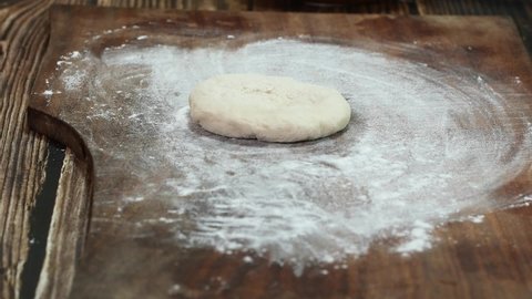 Baker rolling pizza dough on table before baking.Close up male hands rolls out dough using rolling pin cooking pizzeria.Male hands rolling dough